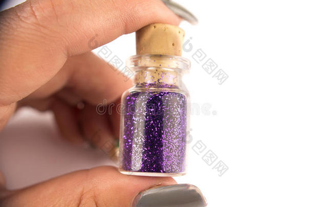 特写手指举起小瓶子容器，里面有紫色的指甲颜色，软木顶部在白色表面
