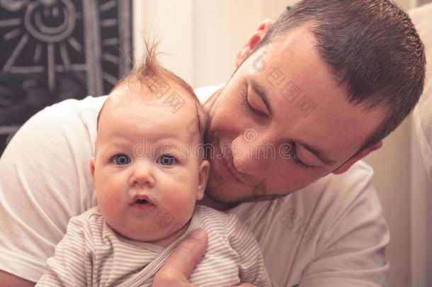 父亲拥抱他的小宝宝。 父亲在看婴儿，婴儿在看相机。 发型有趣的婴儿
