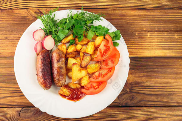 烤肉香肠与油炸土豆，切片西红柿，新鲜农产品和番茄酱在盘子在木制桌子上
