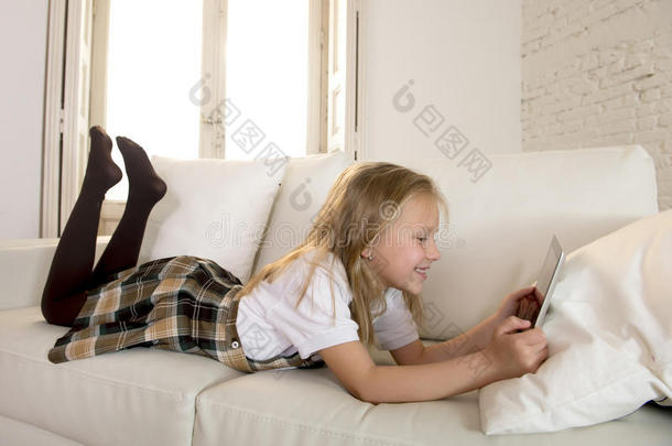 金发<strong>小女孩躺在</strong>家里的<strong>沙发上</strong>，<strong>在</strong>数字平板电脑垫上使用互联网应用程序
