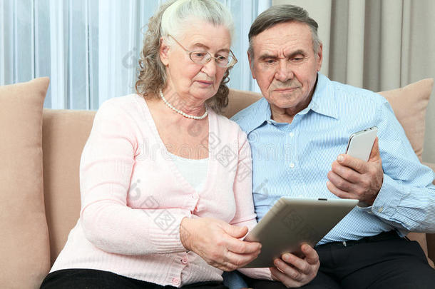 老年人。 一对老年夫妇拿着笔记本电脑、智能手机，在家里舒适的客厅里通过互联网购物