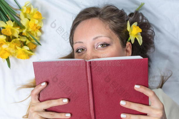 女孩躺在床上，头发上有水仙花，在读一本书