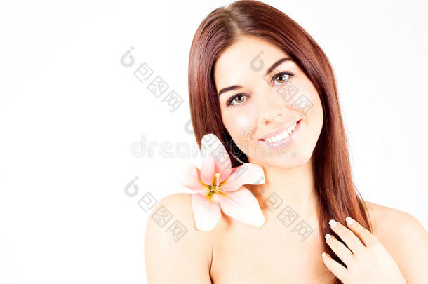 美丽的水疗女人抚摸她的头发。 有粉红色花朵的女人带着洁白的牙齿微笑。 皮肤清新清澈的女人。