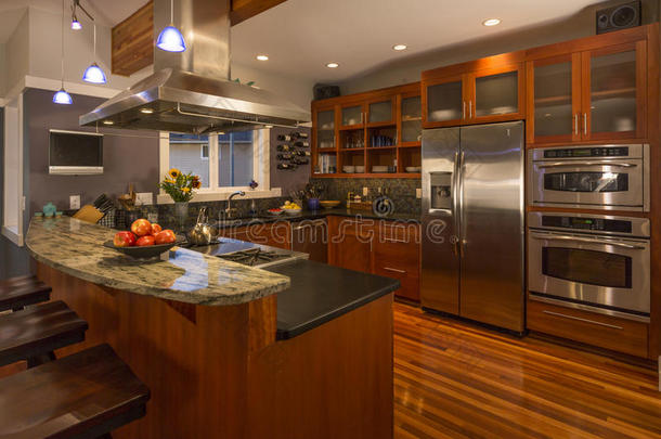 当代高档家庭厨房内部与木柜和地板，花岗岩台面和不锈钢电器