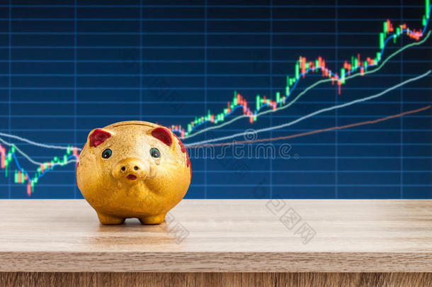 有股票图表背景的木制桌子上的<strong>金猪存钱罐</strong>，