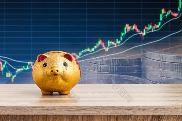 有股票图表背景的木制桌子上的金猪存钱罐，