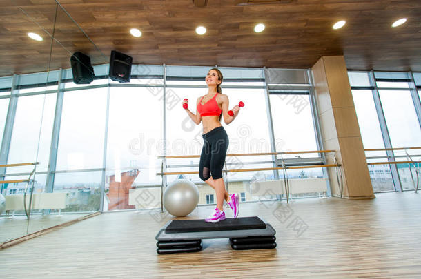 女孩在健身房里用哑铃做踏步有氧运动