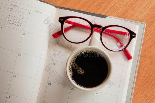 一杯咖啡和眼镜在笔记本上，上面有日历规划师