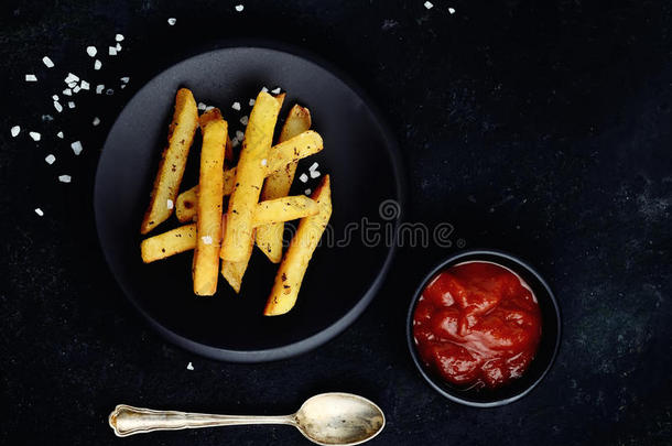 黑碟上的炸薯条，黑色背景上的红酱和老式勺子