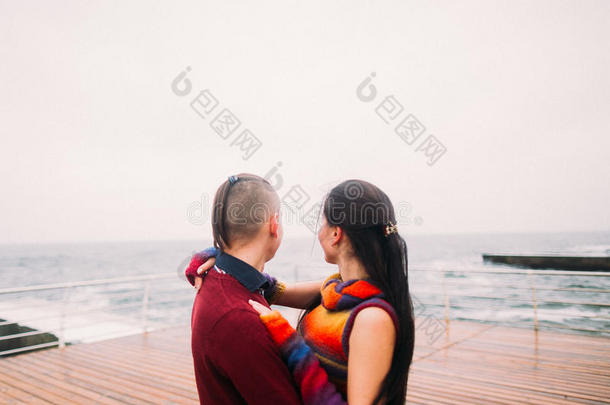 美丽明亮的夫妇梦幻地望着大海。 秋天的雨天，浪漫的蜜月