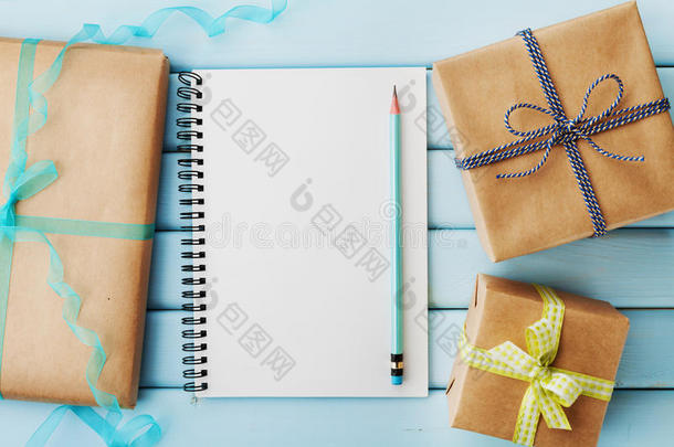 蓝色木桌上用<strong>牛皮纸包装</strong>的空笔记本、铅笔、礼物或礼物盒