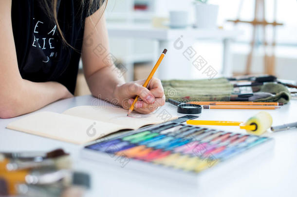 用铅笔在素描簿上画草图的女画家的特写角度视图。 艺术家在艺术工作室写生