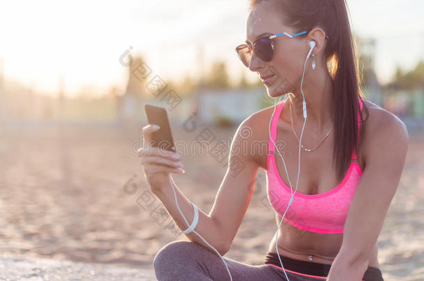 美丽的健身运动员，戴太阳镜的女人，在夏天晚上锻炼后休息，听音乐