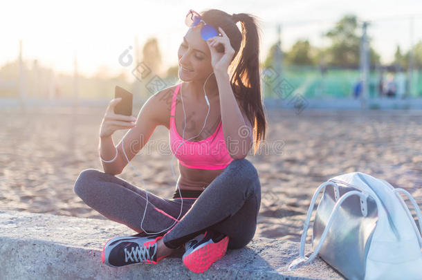 美丽的健身运动员，戴太阳镜的女人，在夏天晚上锻炼后休息，听音乐