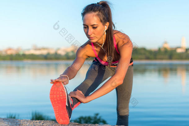 健身<strong>模特</strong>运动员女孩热身伸展她的腿筋，腿和背部。 年轻女子戴着<strong>耳机</strong>锻炼