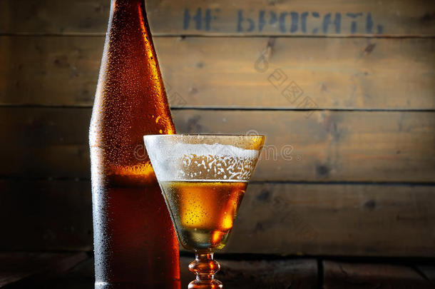 一瓶啤酒和一杯原始形式的啤酒，在木制背景上有泡沫状的冷啤酒