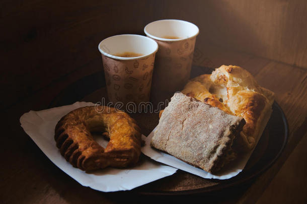 新鲜甜面包面包，两杯牛皮纸杯黑色<strong>咖啡</strong>在纸盘上，木制背景。 <strong>咖啡</strong>休息的概念