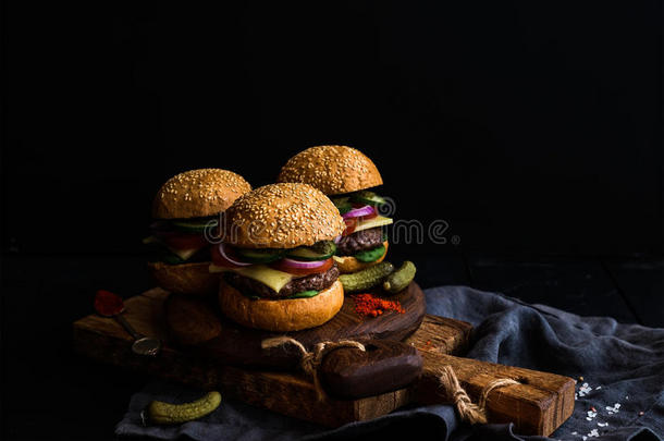 新鲜牛肉汉堡与泡菜和香料在乡村木板，黑色背景。