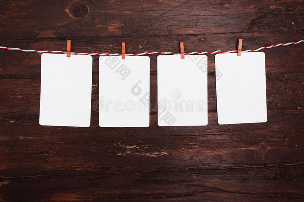 挂在红色条纹晾衣绳上的白纸或相框。 在木制背景上。 文本模板。
