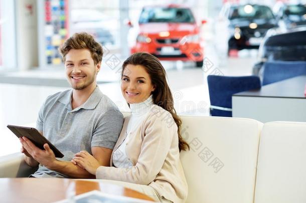 漂亮的年轻夫妇在经销商展厅看着一辆新车。