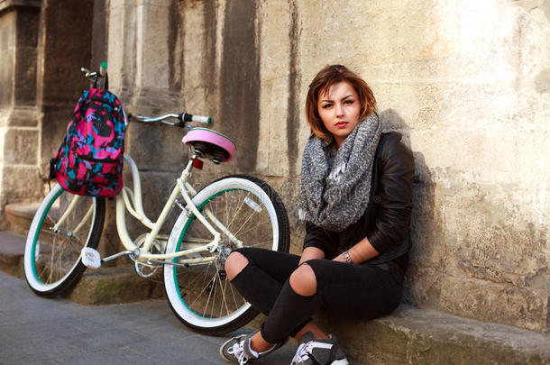 有老式自行车的女孩坐在古建筑的墙上