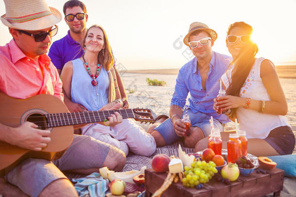 朋友们围坐在海滩上。 一个人在弹吉他