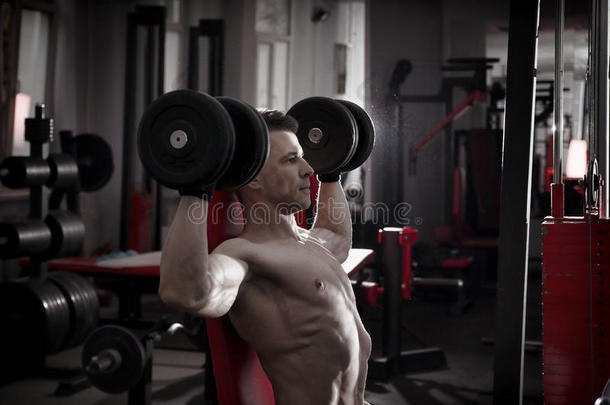 英俊的健美与肌肉躯干锻炼与哑铃在运动长凳在健身房。 完美的肌肉男身体