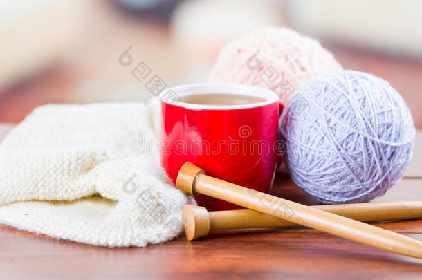 特写白色纱球与针织针和围巾在进行中躺在桌子上，咖啡杯坐在它旁边，模糊
