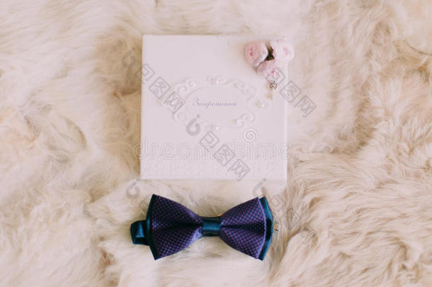 蓝色领结和婚礼邀请卡，白色毛皮背景上有粉红色的小玫瑰