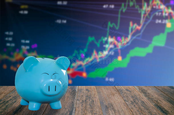 蓝猪银行在木材背景下具有模糊的股票市场背景、金钱和储蓄概念。