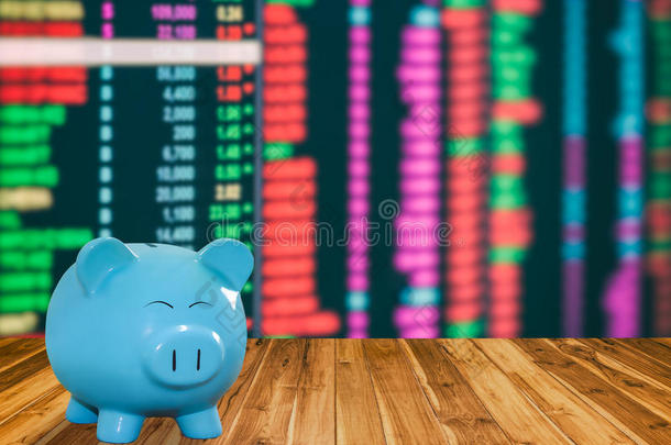 蓝猪银行在木材背景下具有模糊的股票市场背景、金钱和储蓄概念。