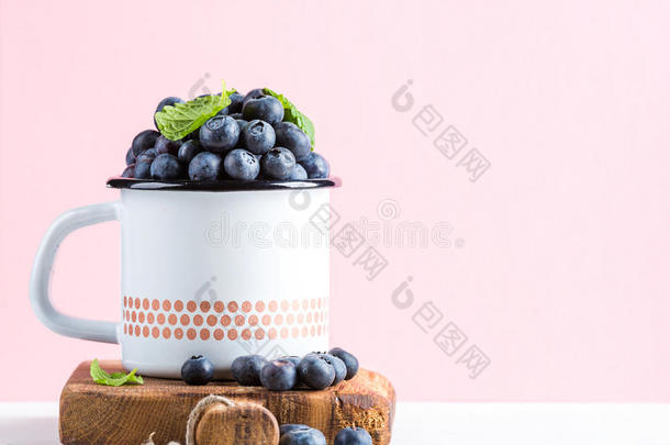新鲜成熟的蓝莓，乡<strong>村风</strong>格的搪瓷杯，在乡村木板上，在柔和的粉红色背景下