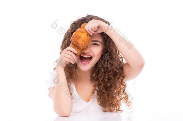 迷人的微笑的年轻女人在桌子上吃羊角面包作为早餐