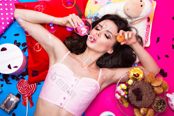 美丽的新鲜女孩娃娃，肥皂泡泡躺在明亮的背景上，周围是糖果、化妆品和礼物