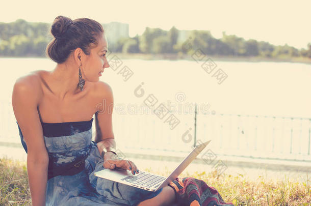 带笔记本电脑的女孩。 坐在草地上有笔记本的漂亮女人