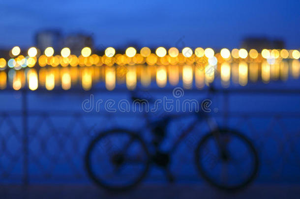 模糊的色调背景与模糊的<strong>城市</strong>灯光与<strong>倒影</strong>在河流和自行车轮廓的桥梁围栏