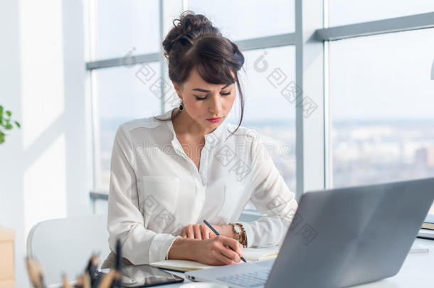 女作家在轻现代办公室<strong>工作</strong>，写下她的笔记本上的新想法，用便携式搜索信息
