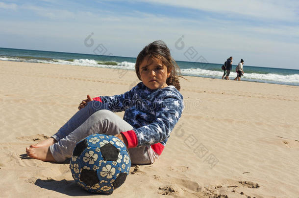 女孩坐在海滩上，在复活节的一个<strong>刮风</strong>的日子里带着一个球。