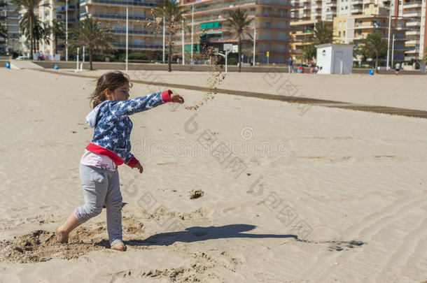 在一个刮风的日子里，女孩在海滩上扔了一团湿沙
