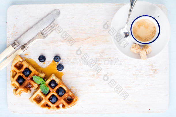 浓缩咖啡杯，柔软的比利时华夫饼，新鲜蓝莓和玛普尔糖浆在白色油漆木板上