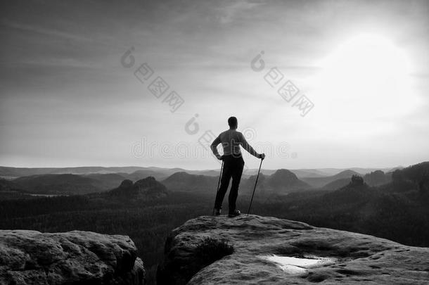 姜发<strong>男子</strong>灰色T恤和<strong>深色</strong>徒步旅行裤子在锋利的岩石上。 游客在雾谷上方有杆。