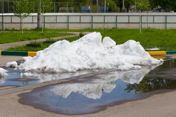 一堆脏雪躺在沥青路上的水坑里