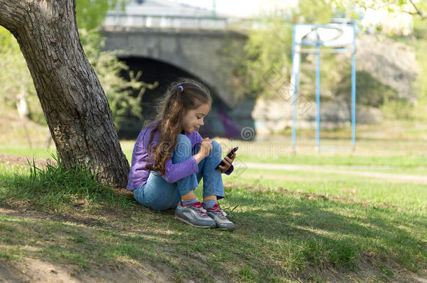 可爱的小女孩坐在草地上，手里拿着手机，用手机发送信息