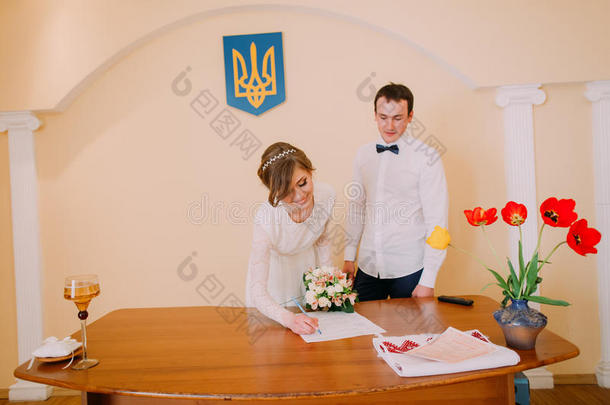 美丽的金发新娘带着新娘花束在登记处签署结婚证书