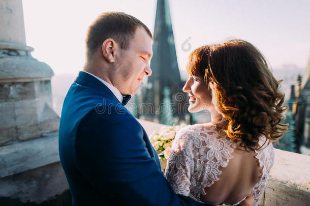 温柔美丽的新娘和新郎双手捧着花束在古老的阳台上互相看着，特写