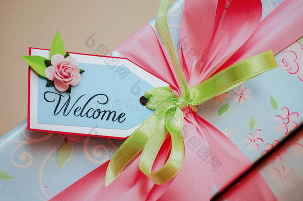 带欢迎卡的礼品包装盒。 浅蓝色的纸和淡粉色的玫瑰。