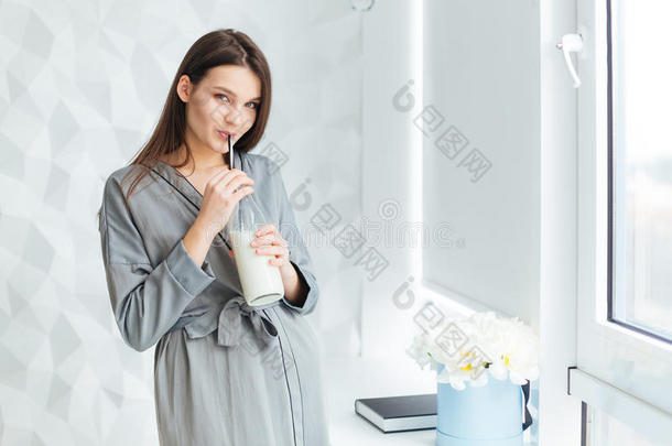 穿着浴袍的迷人女人用吸管喝牛奶泡沫瓶
