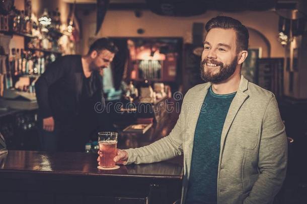 快乐的男人在电视上看足球比赛，在酒吧的酒吧柜台喝生啤酒。