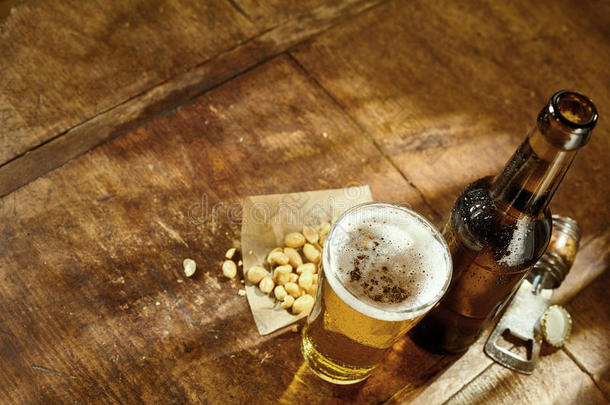 一杯啤酒放在桌子上，开瓶器和花生