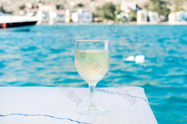 海滩<strong>餐厅</strong>桌上的一杯白葡萄酒，背景是<strong>海景</strong>、碧水和游艇